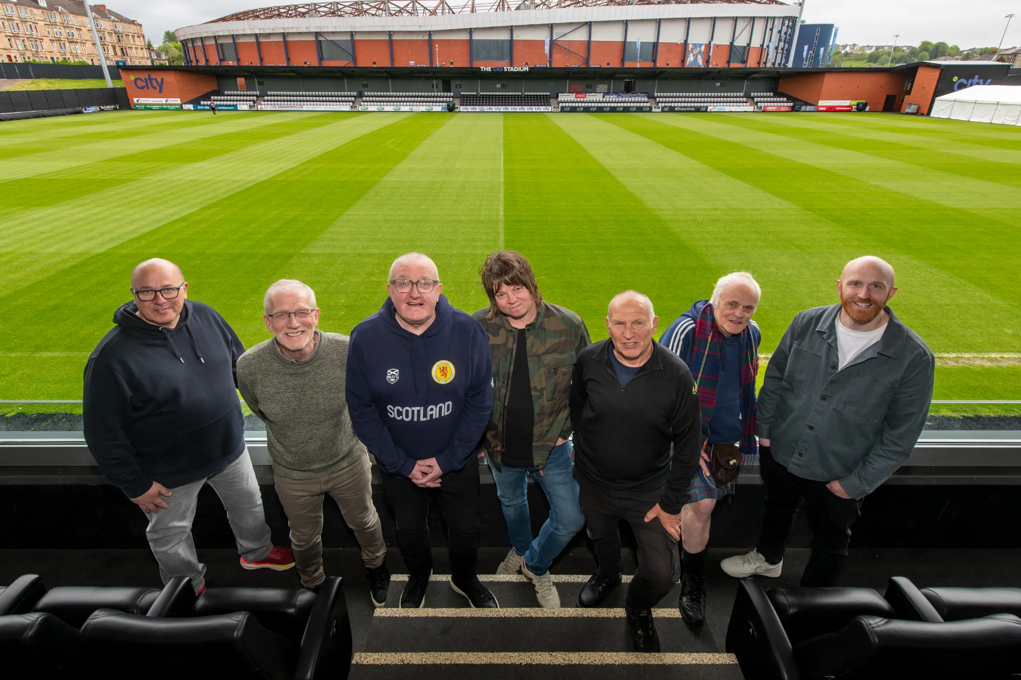 L to R: David Sheret, Richard Gordon, Tam Cowan, Terry McDermott, Paul Goodwin, Ted Christopher, Ray Bradshaw. Queens Park’s City Stadium with Hampden Park behind.